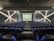 A modern theater with rows of blue and black seats facing a stage. The walls have geometric patterns with illuminated lines creating an 'X' shape. The stage is empty except for a few people standing near the back.