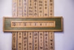 A wooden framed artwork displaying the word 'Digital' in blue letters set against a muted green background. Vertical panels in the background contain various combinations of letters and phonetic symbols in blue on a beige surface.