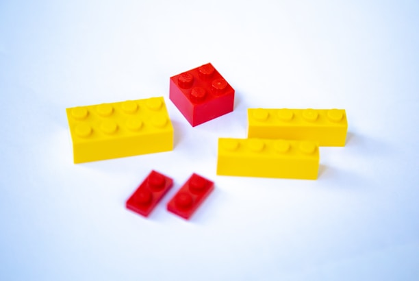 Several LEGO bricks are arranged on a white surface, including rectangular yellow blocks and smaller red blocks.