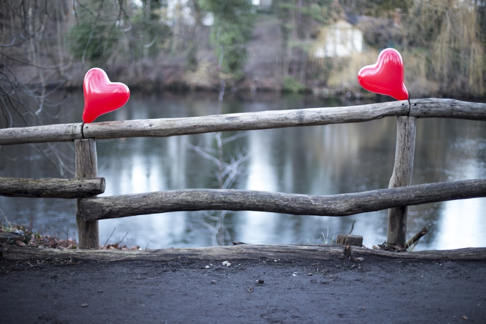 two red hearts sitting on top of a wooden fence