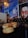 A dimly lit restaurant scene featuring two burgers with sesame seed buns and melted cheese on a small table. The background includes a vibrant wall mural depicting a street scene and a stylized portrait of a person wearing sunglasses. A sign on the wall indicates no smoking.