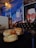A dimly lit restaurant scene featuring two burgers with sesame seed buns and melted cheese on a small table. The background includes a vibrant wall mural depicting a street scene and a stylized portrait of a person wearing sunglasses. A sign on the wall indicates no smoking.
