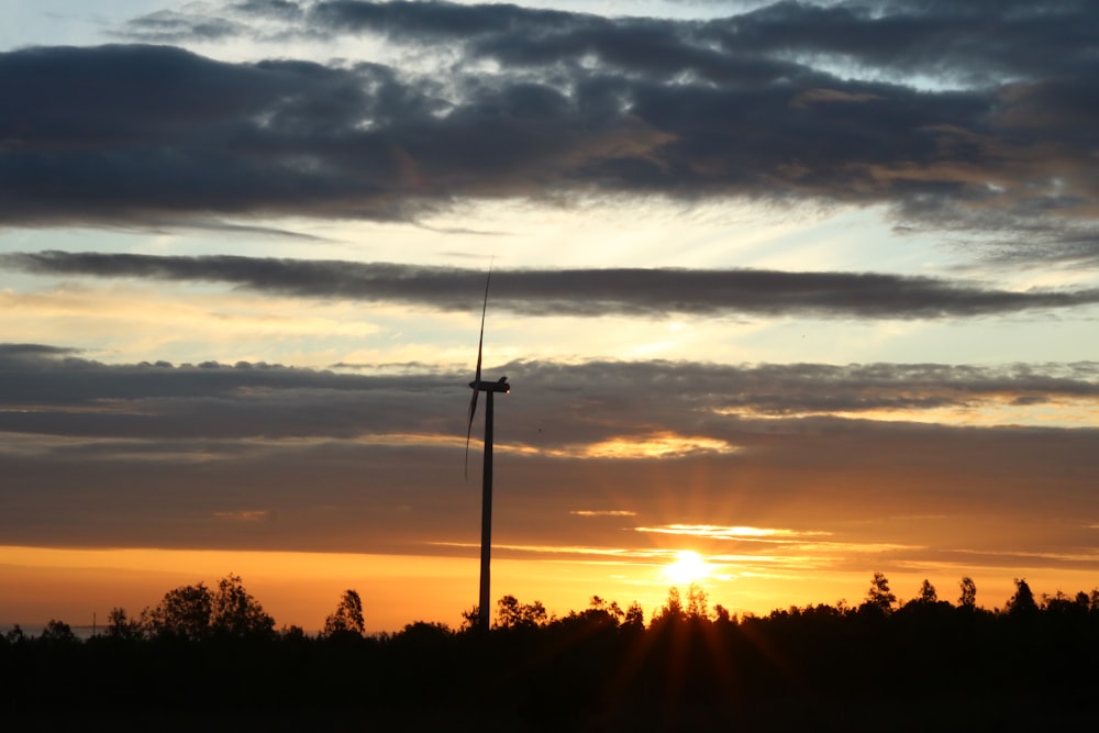 the sun is setting behind a wind turbine