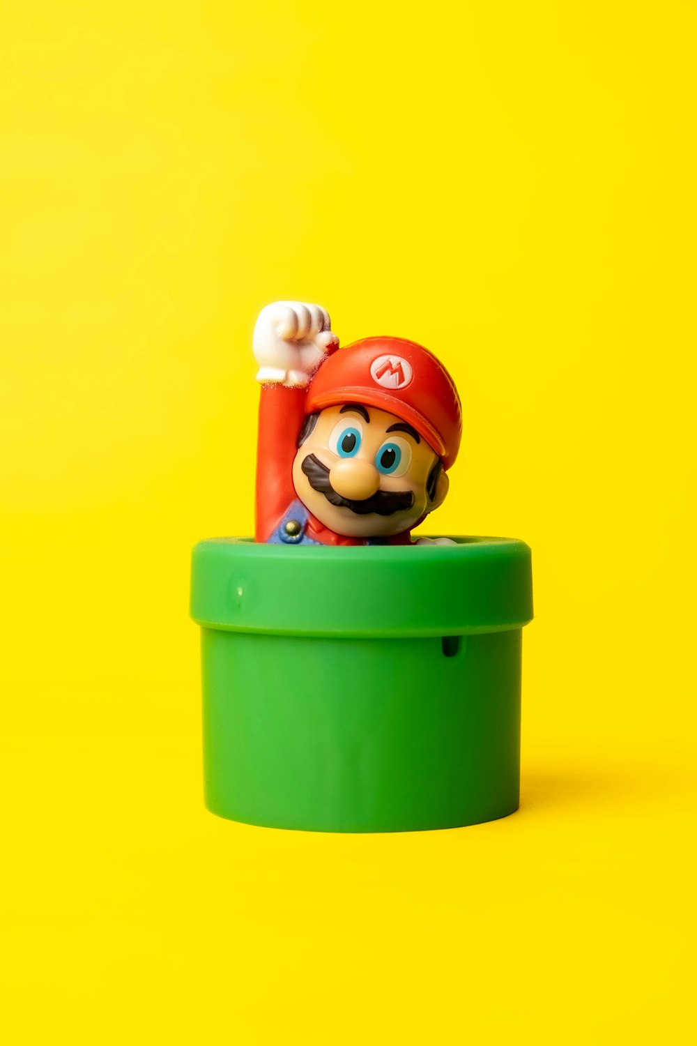 Un Mario de juguete en un contenedor verde sobre un fondo amarillo