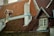 The image features a series of steeply pitched roofs with red clay tiles and wooden accents. There is a prominent white chimney, flanked by weathered roofing. A window with detailed wood framing is visible, hinting at a rustic architectural style.