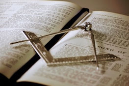 An open ancient Masonic book resting on a polished wooden table under warm light.