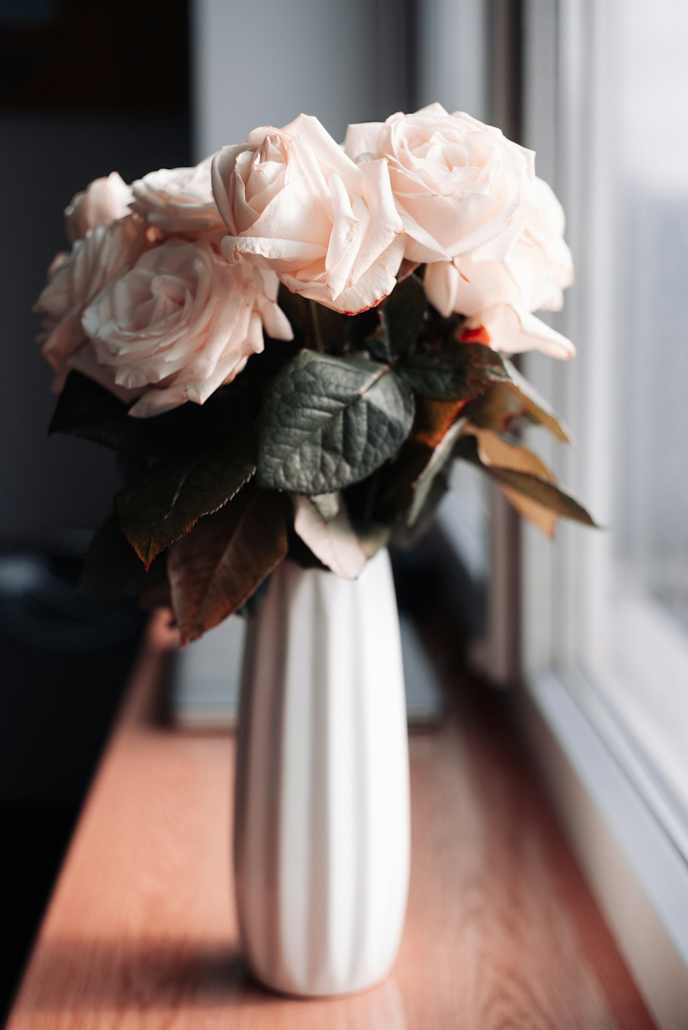 a white vase filled with pink flowers on a window sill