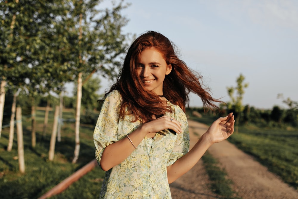 a woman standing on a dirt road holding a cell phone