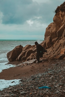 A solitary figure standing on a rocky shore under a brooding gray sky.