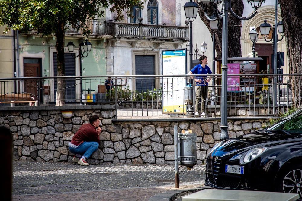 a man sitting on the ground next to a stone wall