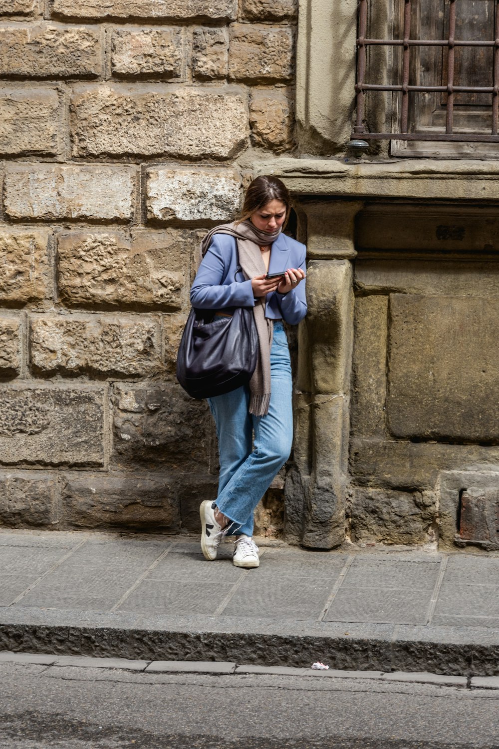 a woman leaning against a stone wall using a cell phone
