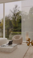 Spacious, minimalist living room featuring floor-to-ceiling windows and gold accents.