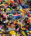 A colorful assortment of keychains and small plastic figurines featuring various cartoon characters and designs. The items are packed closely together, creating a vibrant and chaotic visual effect. Among the collection, there are wristbands, toys, and a variety of character-themed accessories.
