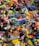 A colorful assortment of keychains and small plastic figurines featuring various cartoon characters and designs. The items are packed closely together, creating a vibrant and chaotic visual effect. Among the collection, there are wristbands, toys, and a variety of character-themed accessories.