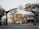 An archway on a street marks the entrance to Ottawa St., featuring a large clock at the center. The street is lined with small businesses and trees, with few people walking around. The area has an inviting and peaceful feel, typical of a small town or community street.