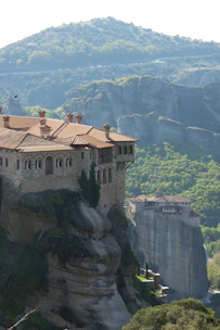 An ancient monastery nestled among green hills with colorful wildflowers in the foreground.