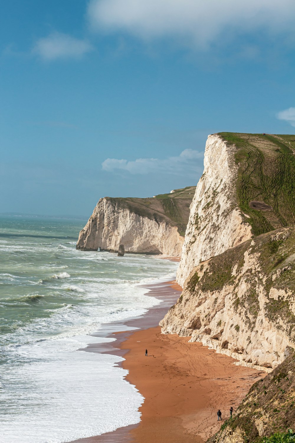 a sandy beach next to the ocean with a cliff in the background