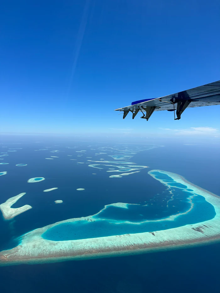 Aerial view of a seaplane wing over turquoise atolls, similar to island-hopping the Out Islands
