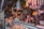 A bustling deli or market stall with an array of cured meats hanging overhead. The counter is filled with a variety of cheeses and meats, while shelves in the background store jars and condiments. The space is dimly lit, creating a cozy and inviting atmosphere.
