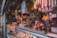 A bustling deli or market stall with an array of cured meats hanging overhead. The counter is filled with a variety of cheeses and meats, while shelves in the background store jars and condiments. The space is dimly lit, creating a cozy and inviting atmosphere.