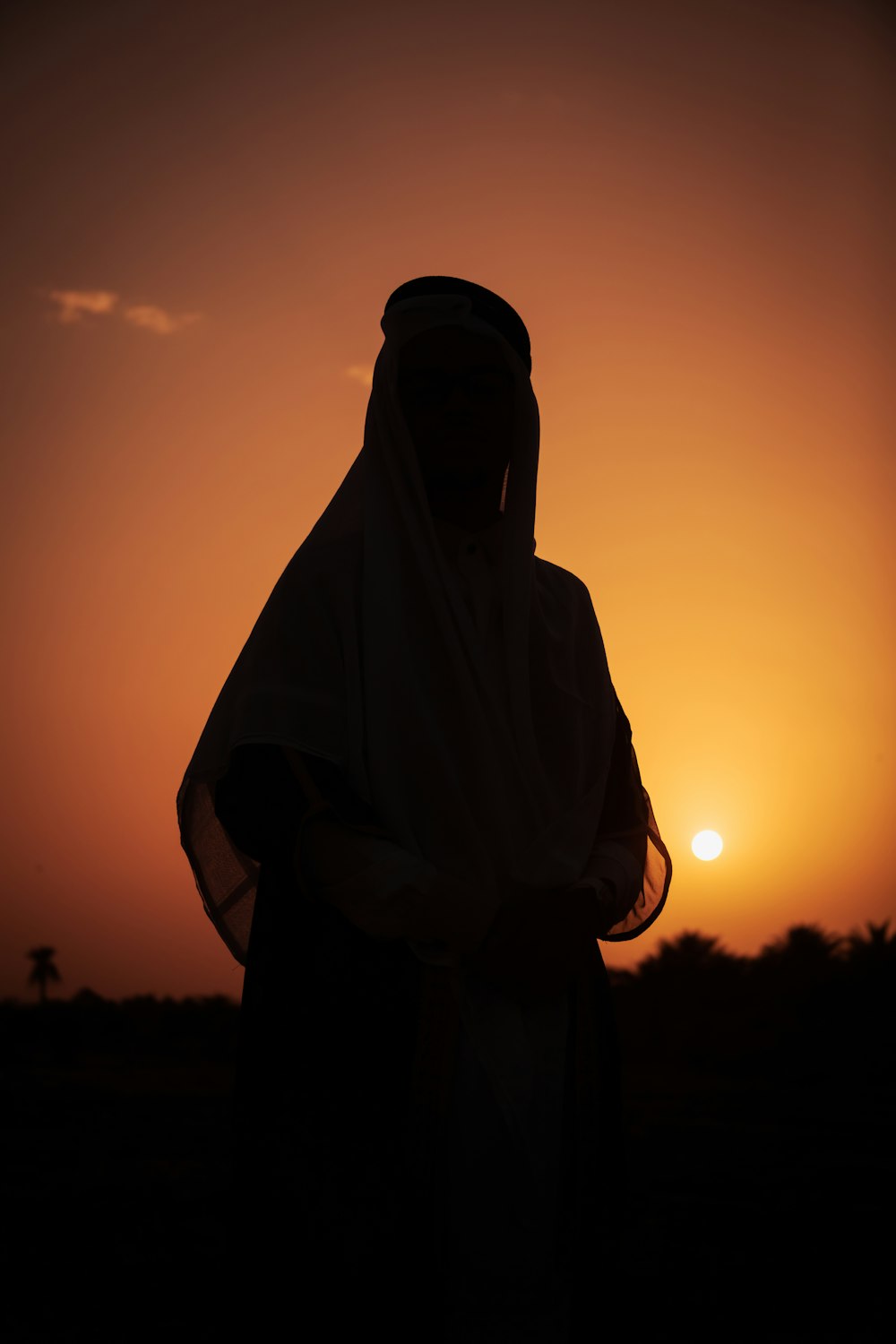 a silhouette of a person wearing a veil at sunset