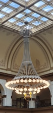 A skilled technician carefully installing a sparkling chandelier in a vaulted ceiling room bathed in natural light.