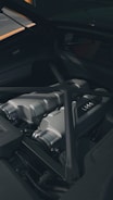 A close-up view of a sleek, metallic car engine compartment with visible parts including intake manifolds and reinforced bars. The area is clean and well-maintained, showcasing modern engineering design.