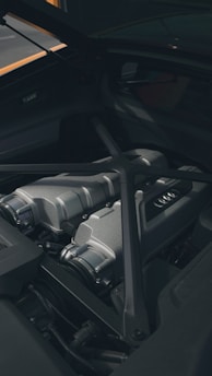 A close-up view of a sleek, metallic car engine compartment with visible parts including intake manifolds and reinforced bars. The area is clean and well-maintained, showcasing modern engineering design.