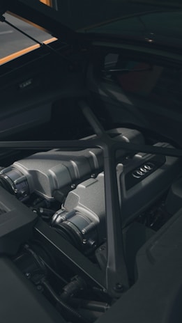 A close-up view of a sleek, metallic car engine compartment with visible parts including intake manifolds and reinforced bars. The area is clean and well-maintained, showcasing modern engineering design.