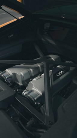 A close-up view of a sleek, metallic car engine compartment with visible parts including intake manifolds and reinforced bars. The area is clean and well-maintained, showcasing modern engineering design.