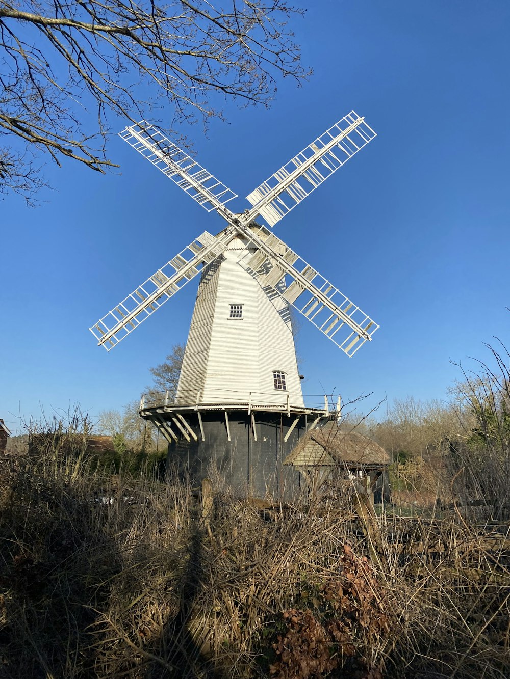 a white windmill sitting in a field next to a tree