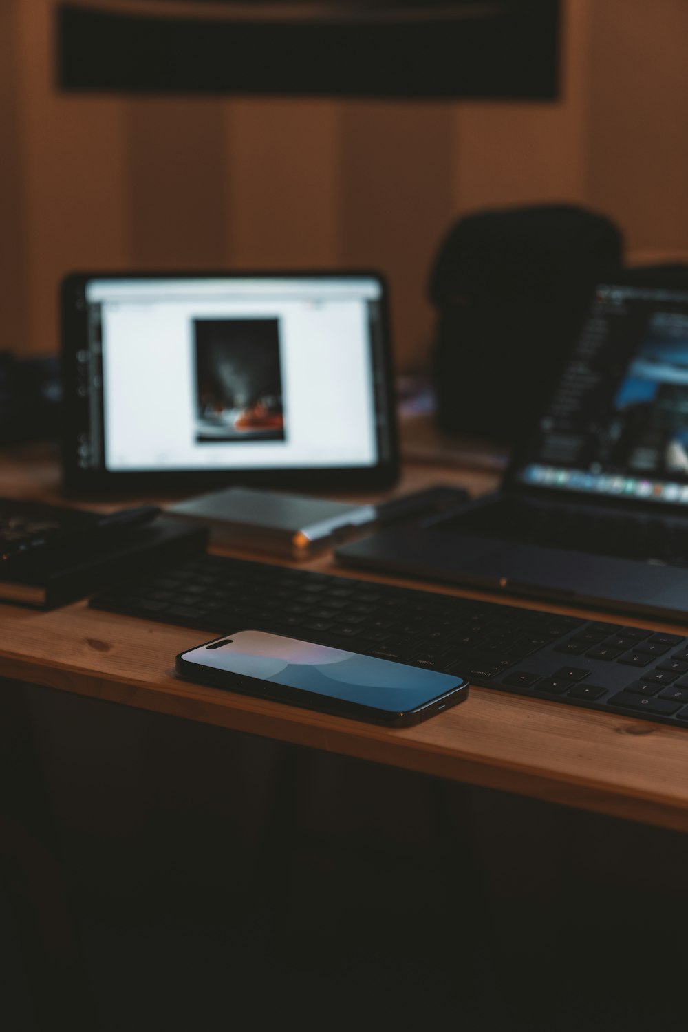 a wooden desk topped with two laptops and a phone