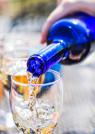 Close-up of a hand pouring wine into a glass with the ocean waves softly blurred in the background.