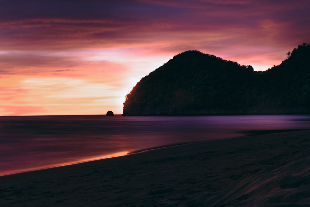 a sunset on a beach with a mountain in the distance