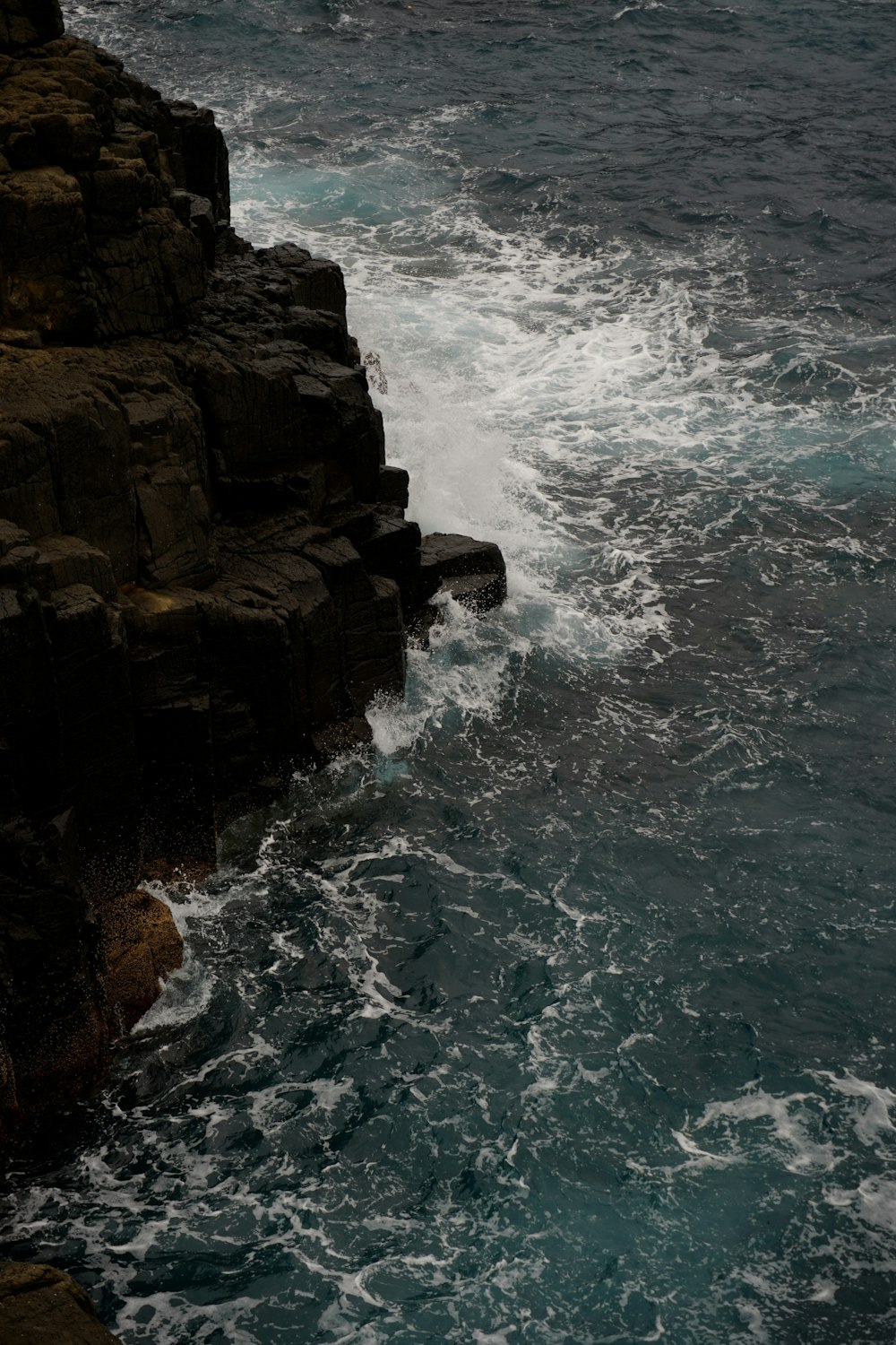 a bird flying over the ocean next to a rocky cliff