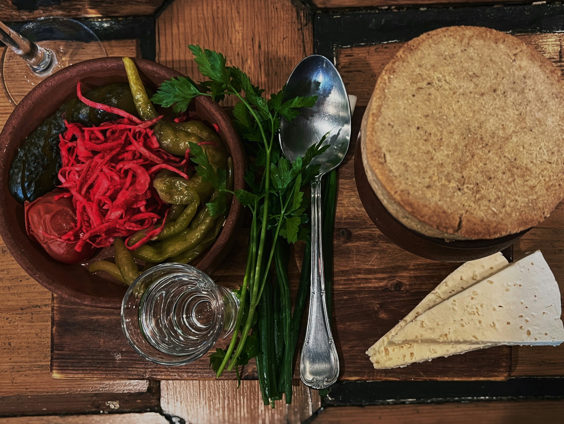 A rustic wooden table adorned with jars of colorful homemade pickles and a bottle of cold-pressed oil, surrounded by fresh vegetables.