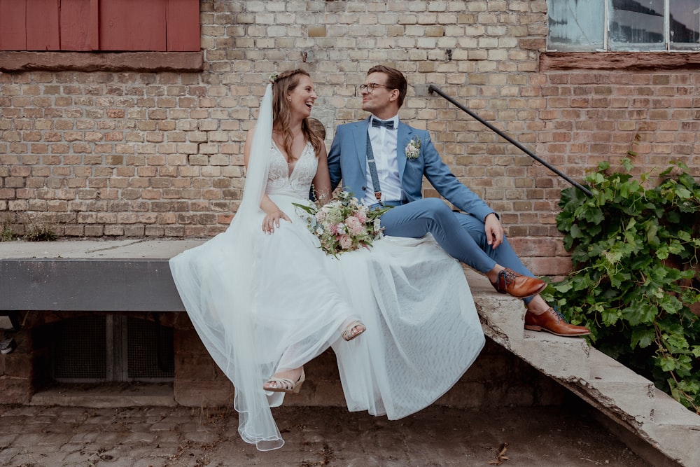 a bride and groom sitting on a bench in front of a brick building