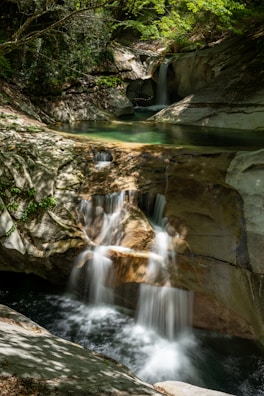 A cascading waterfall pouring into a clear pool with sunlight filtering through trees.