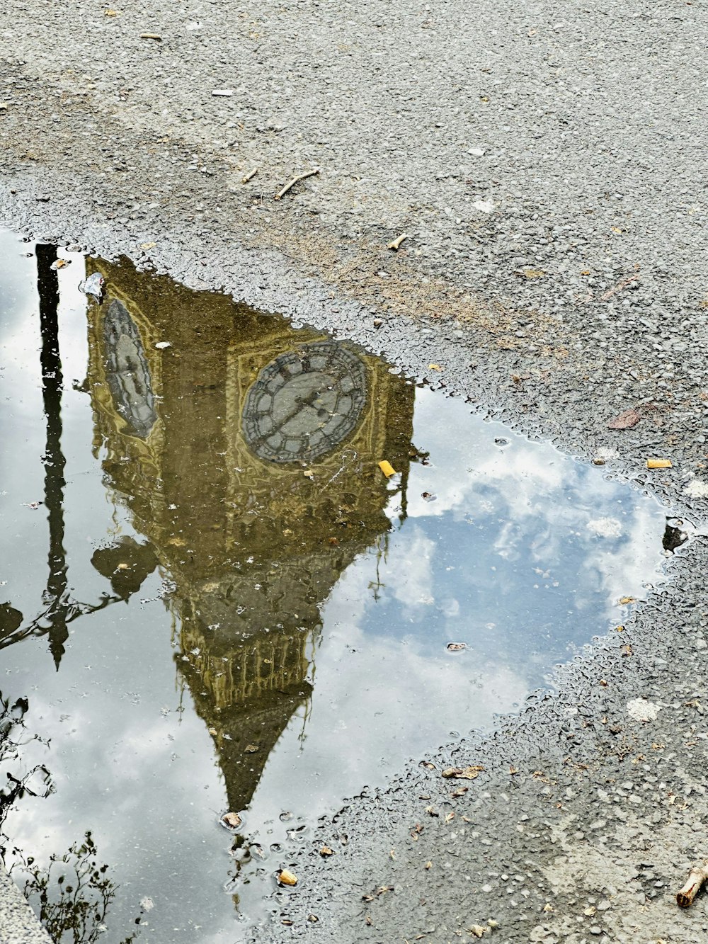 a reflection of a clock tower in a puddle of water