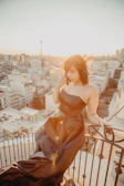 A sensual woman in elegant evening wear posing on a Parisian balcony at sunset.