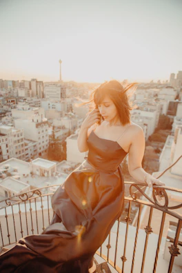 A sensual woman in elegant evening wear posing on a Parisian balcony at sunset.