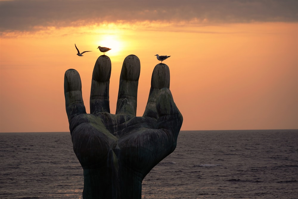 una estatua de una mano con dos pájaros encima