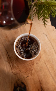 Close-up of steaming organic coffee being poured into a rustic ceramic cup on a wooden table with soft natural light.