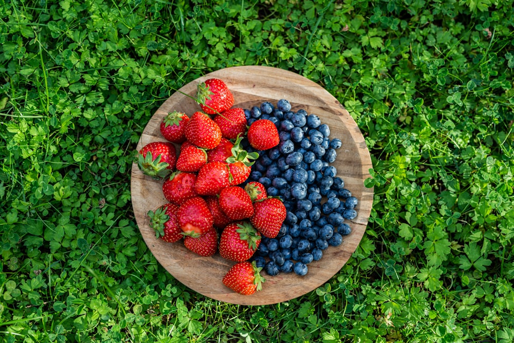 strawberries and blueberries on a wooden plate on green grass