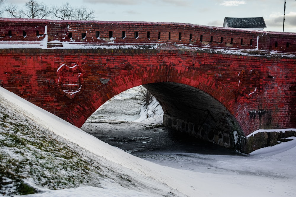 a red brick bridge over a river with snow on the ground