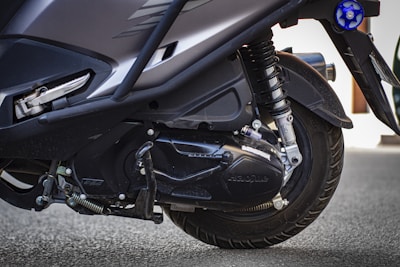 Close-up view of the rear wheel and suspension system of a scooter, highlighting the tire treads, shock absorber, and parts of the engine cover.