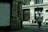 A street view featuring a large building labeled 'Victoria House' with ornate architectural features. Several people are walking on the sidewalk in front of the building, including one person in a white shirt walking away from the camera. A police car is parked on the side of the road.