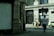 A street view featuring a large building labeled 'Victoria House' with ornate architectural features. Several people are walking on the sidewalk in front of the building, including one person in a white shirt walking away from the camera. A police car is parked on the side of the road.