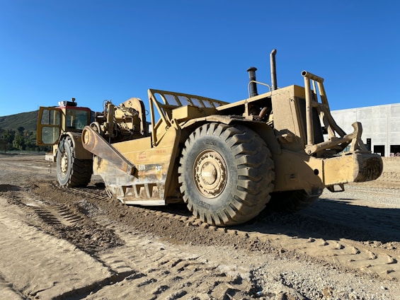 A heavy-duty dump truck loaded with construction materials driving on a busy construction site under a clear blue sky.
