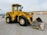 A large yellow front loader with the number 950B displayed on the side is parked on a gravel lot. The machinery has big thick tires and a sizeable bucket, which shows signs of wear and some soil residue. In the background, there are distant construction materials and a hilly landscape under an overcast sky.